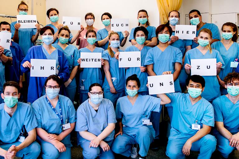 Gruppenbild von Stationspersonal mit dem Aufruf, während der Coronapandemie zuhause zu bleiben