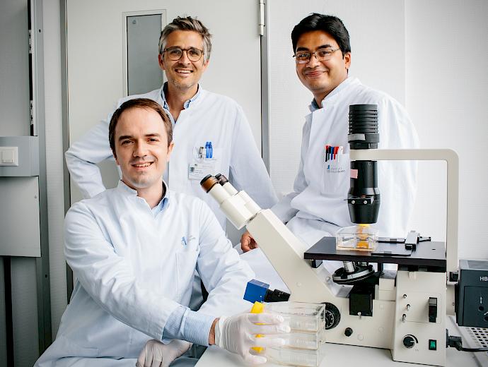 Drei Forscher des Herzzentrums in Laborkitteln schauen lächelnd in die Kamera